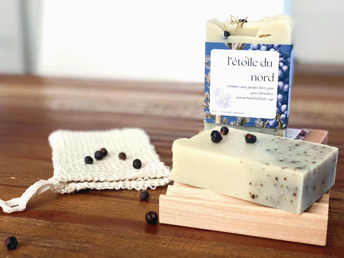 l'etoile du nord soap on a wooden table with dried juniper berries sprinkled on top.