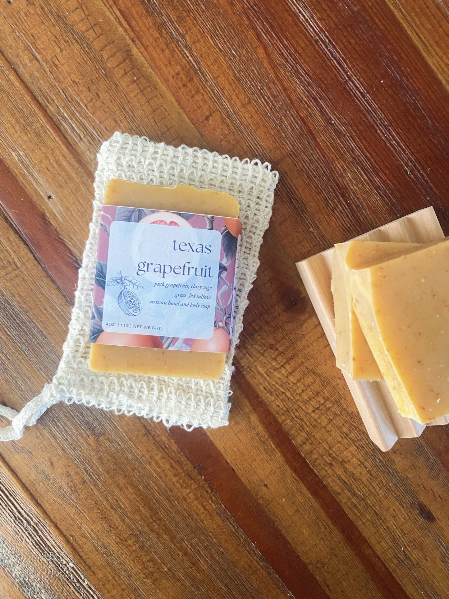 texas grapefruit soap bar with product labeling on a sisal soap saver drawstring bag. this is on top of a wooden table.