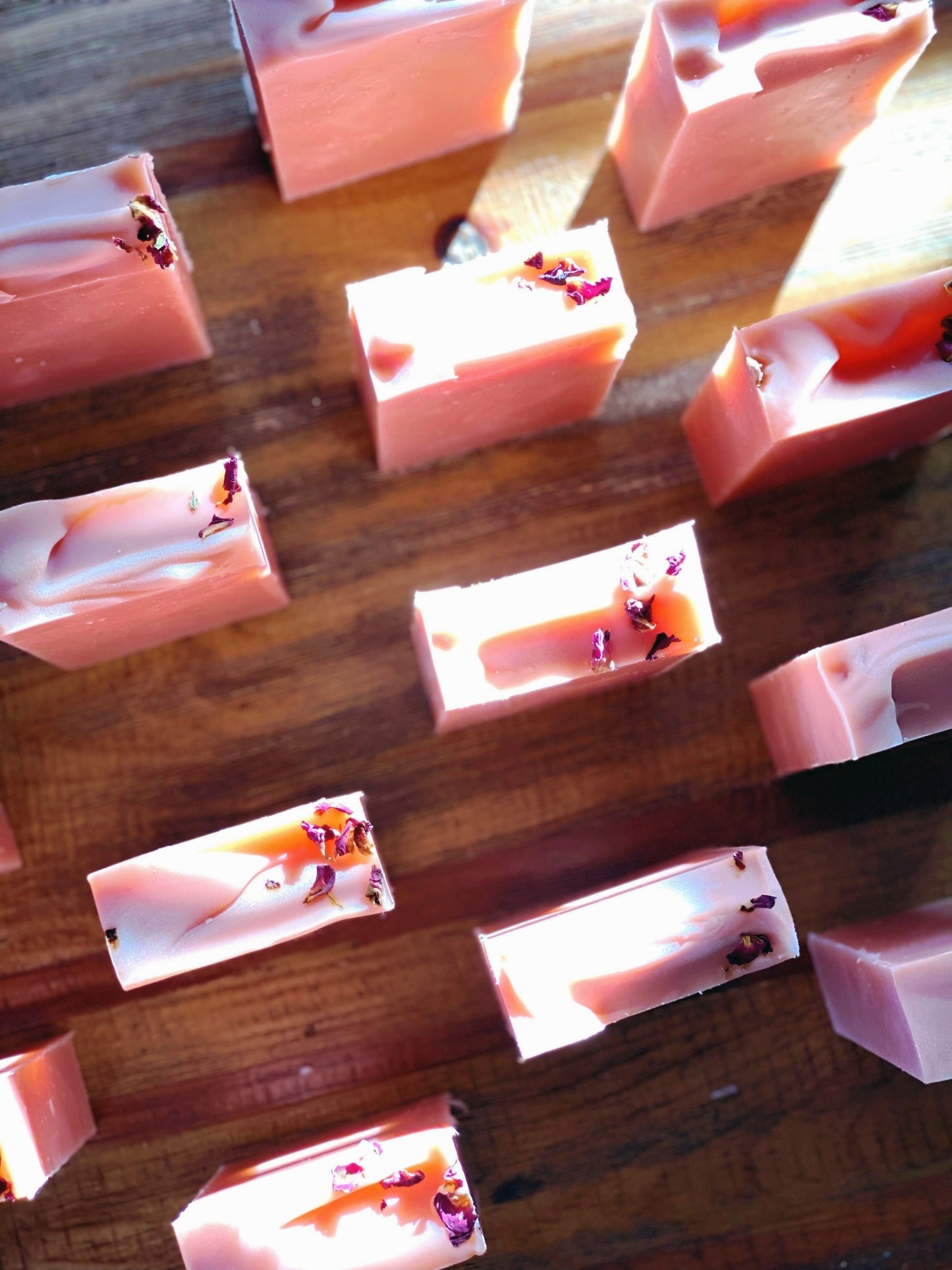 overhead view of 11 coconut and rose soaps on a wooden table.