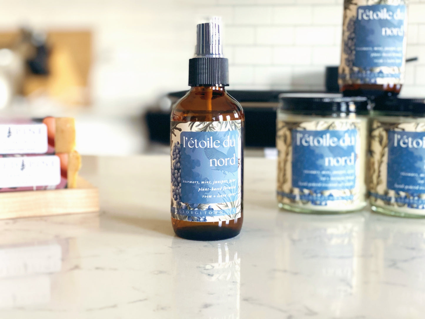 glass spray bottle of l'etoile du nord room and linen spray on a quartz counter in a white kitchen. there are texas grapefruit soaps and l'etoile du nord candles in the background.