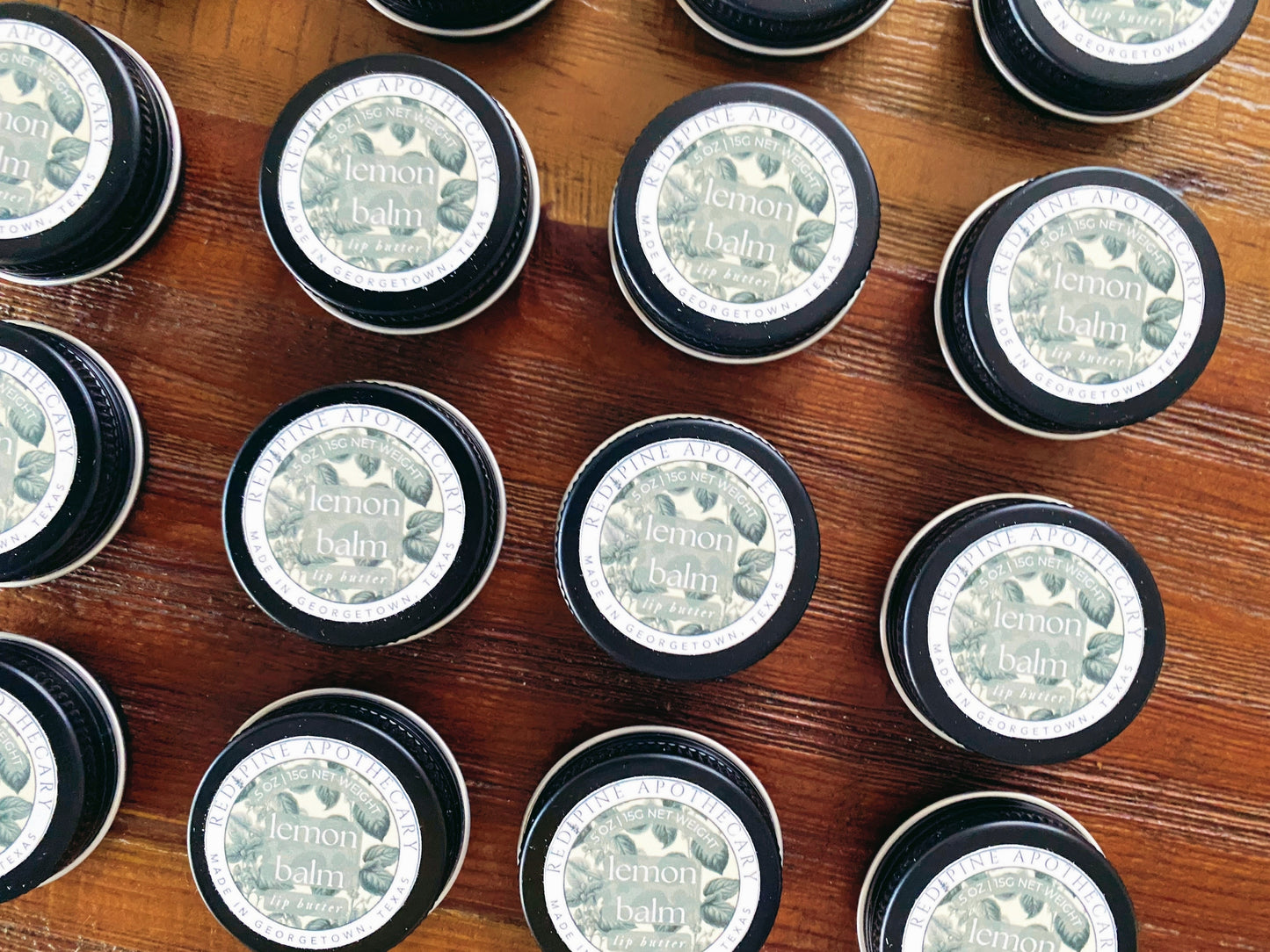 brown table with 10 lemon balm lip butter tins laying down on top.
