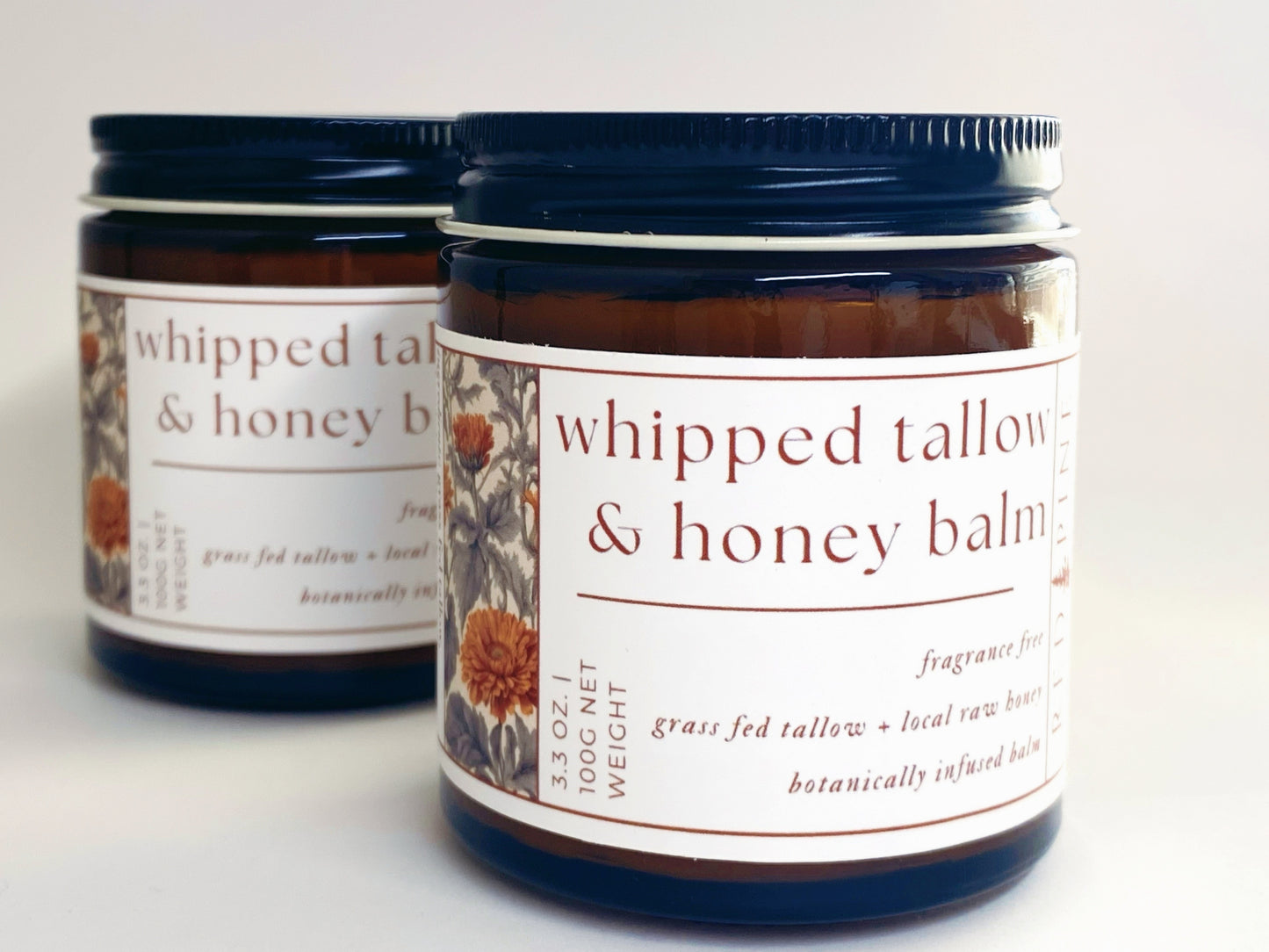 two glass jars of whipped tallow and honey balm against a white backdrop.